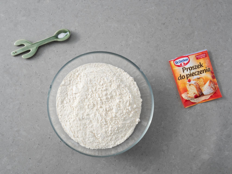 W miseczce mąka pszenna. Obok proszek do pieczenia i sól na łyżeczce.