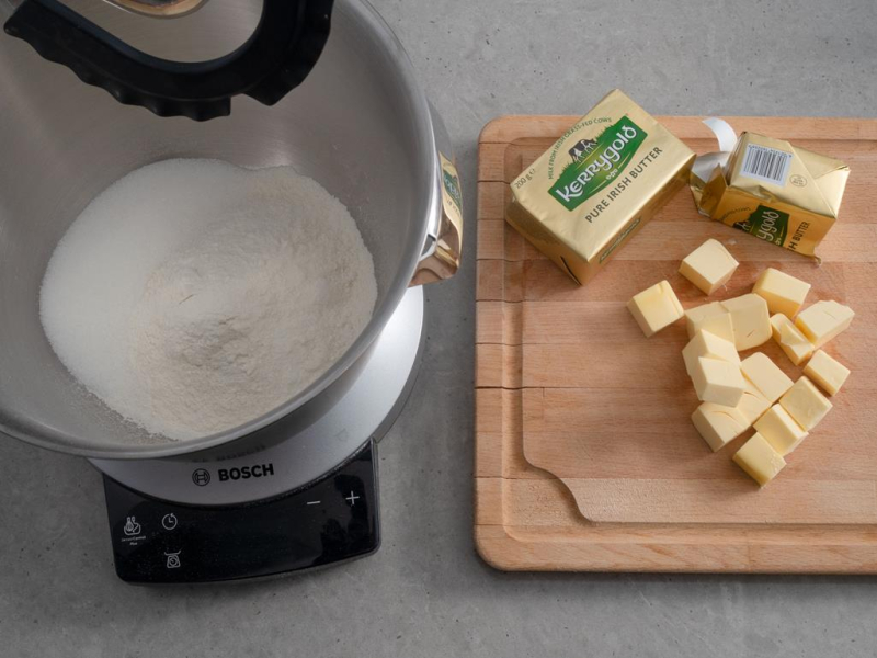 na drewnianej desce pokrojone w kostkę masło Kerrygold w misie suche składniki na kruszonkę
