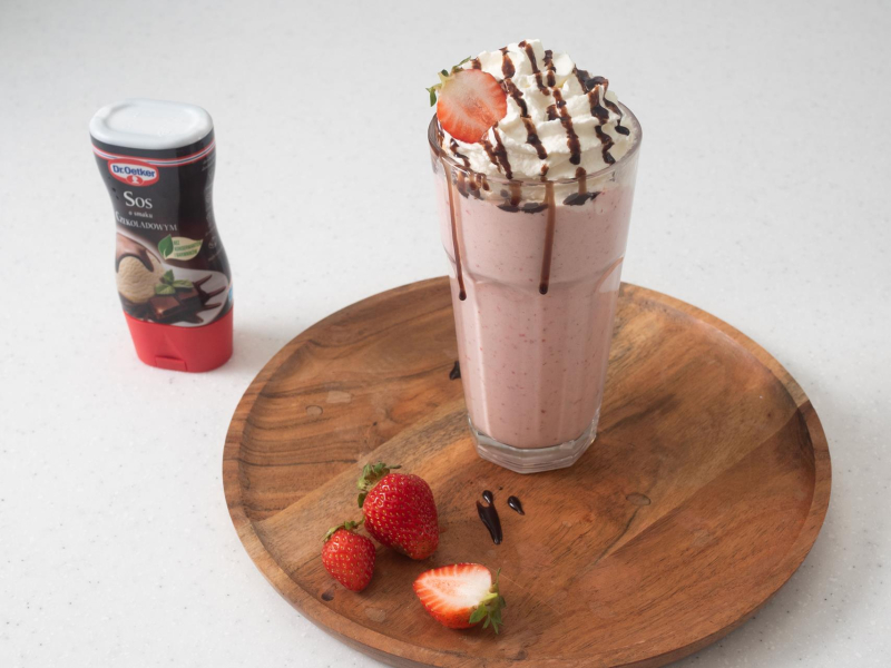 Shake truskawkowy udekorowany bitą śmietaną i sosem czekoladowym.