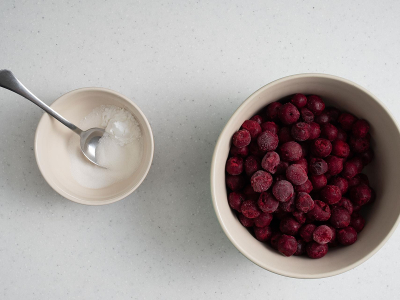 W dużej misie mrożone wiśnie. Obok w miseczce wymieszany cukier z mąką ziemniaczaną.