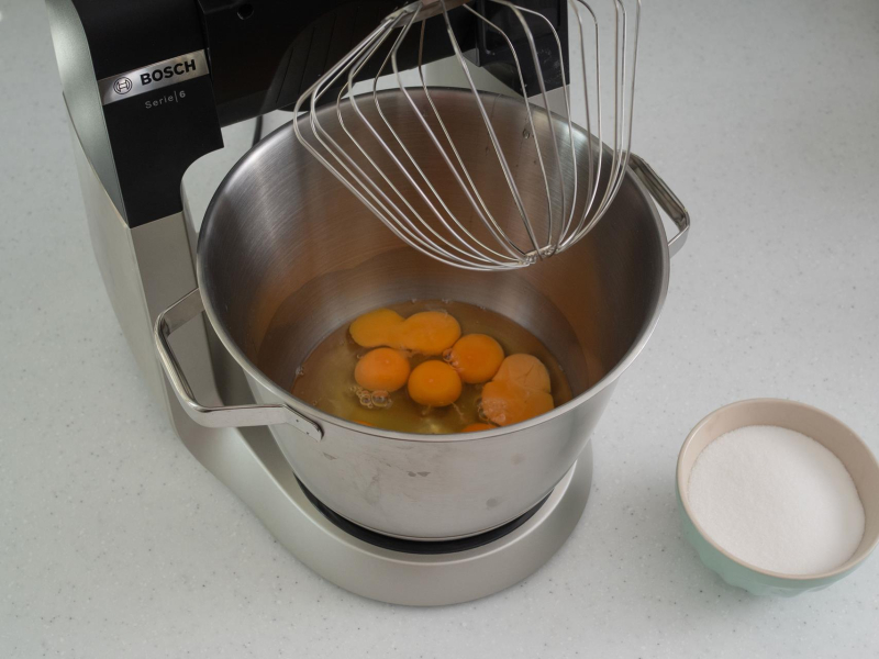 Jajka w misie robota kuchennego. Obok cukier w misce.