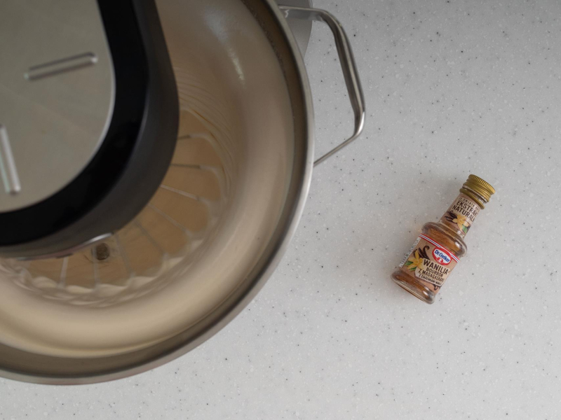 Utarte jajka z cukrem w misie, a obok opakowanie ekstraktu z wanilii.