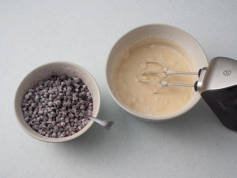 w misce zmiksowane ciasto mikserem obok  miska z oprószonymi mąką jagodami