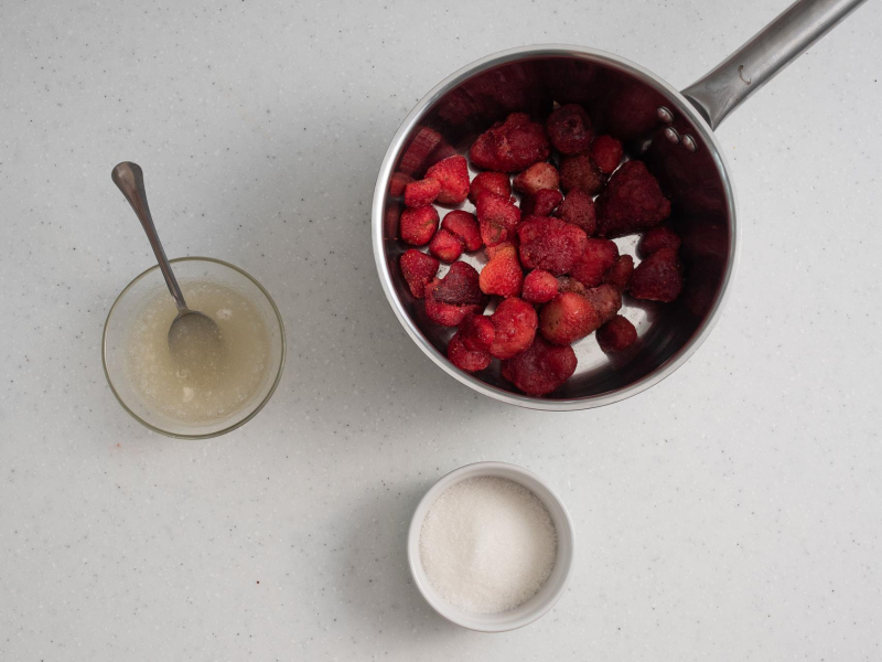 W garnku truskawki. Obok napęczniała żelatyna i cukier w miseczce.