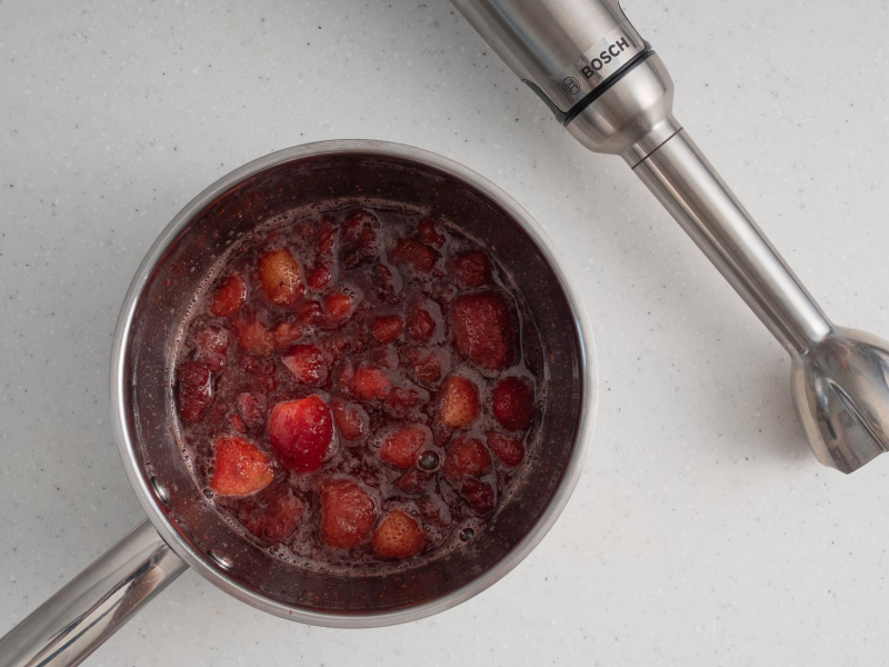 W garnku zagotowane owoce. Obok blender ręczny.