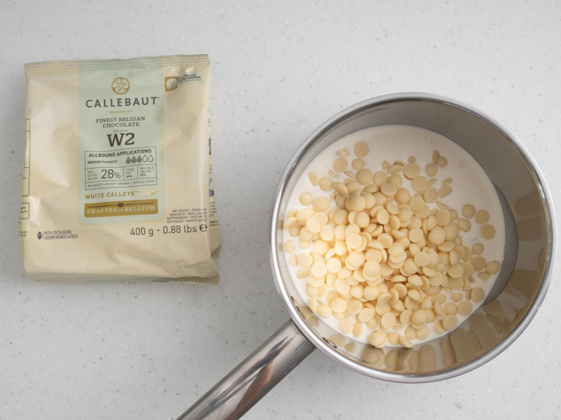 Na blacie opakowanie białej czekolady i garnek ze śmietanką i białą czekoladą.