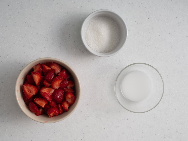 W miseczce truskawki, obok cukier i rozmieszana w wodzie mąka ziemniaczana.