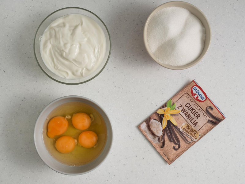 Na blacie kuchennym jajka, cukier z wanilią, cukier oraz jogurt.