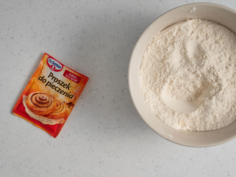 W misie mąka, obok opakowanie proszku do pieczenia.
