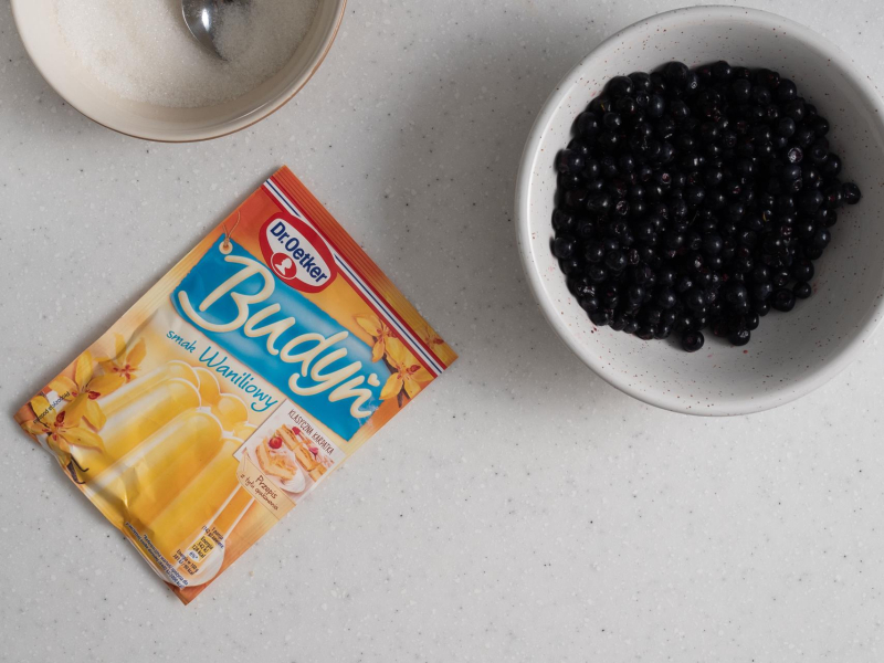 Na blacie kuchennym jagody w miseczce oraz opakowanie budyniu waniliowego.