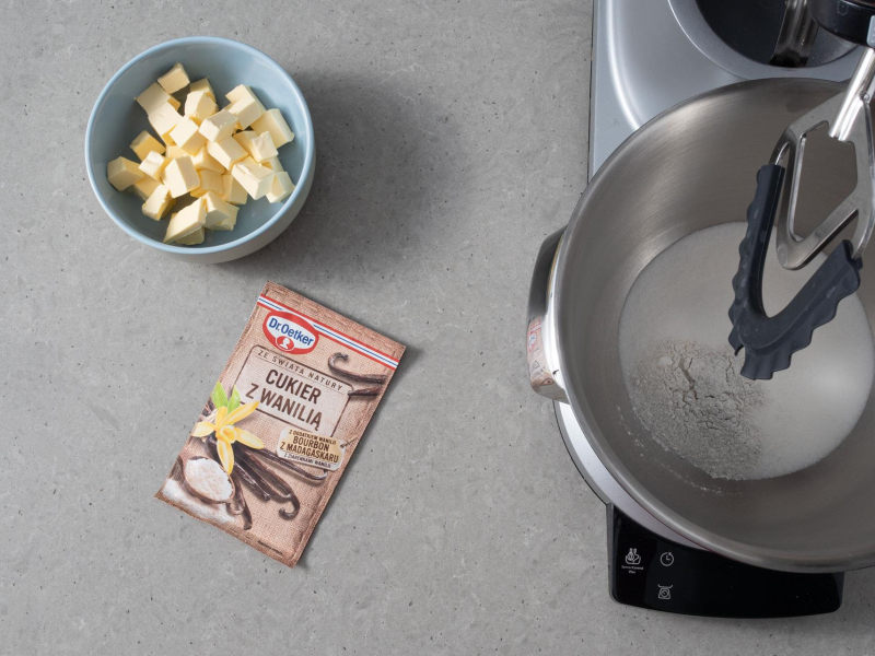 Na blacie kuchennym cukier z wanilią, kostki masła roślinnego i cukier w misie kuchennej.
