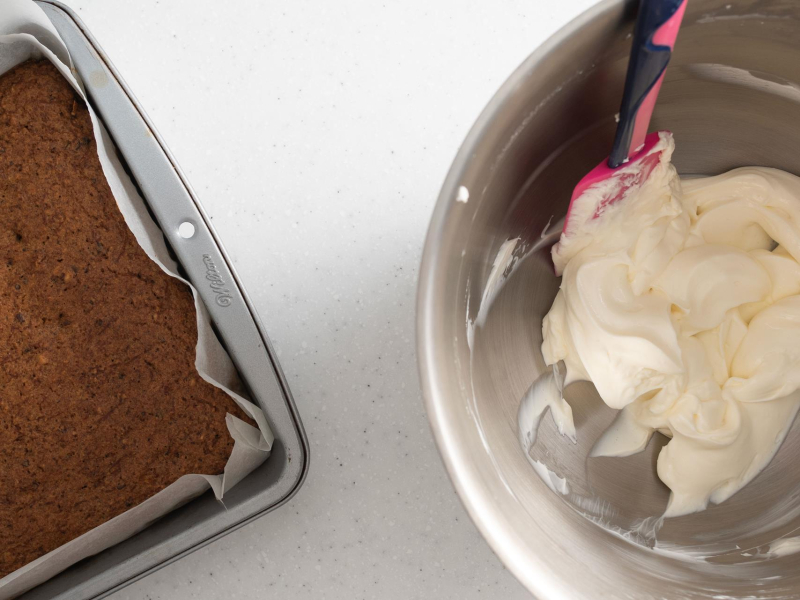 Upieczone ciasto marchewkowe na blacie, a obok serek śmietankowy utarty z erytrytolem.