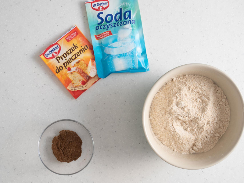 W jednej misie wymieszane suche składniki do ciasta. Obok opakowanie proszku do pieczenia, sody oraz wymieszane przyprawy korzenne.