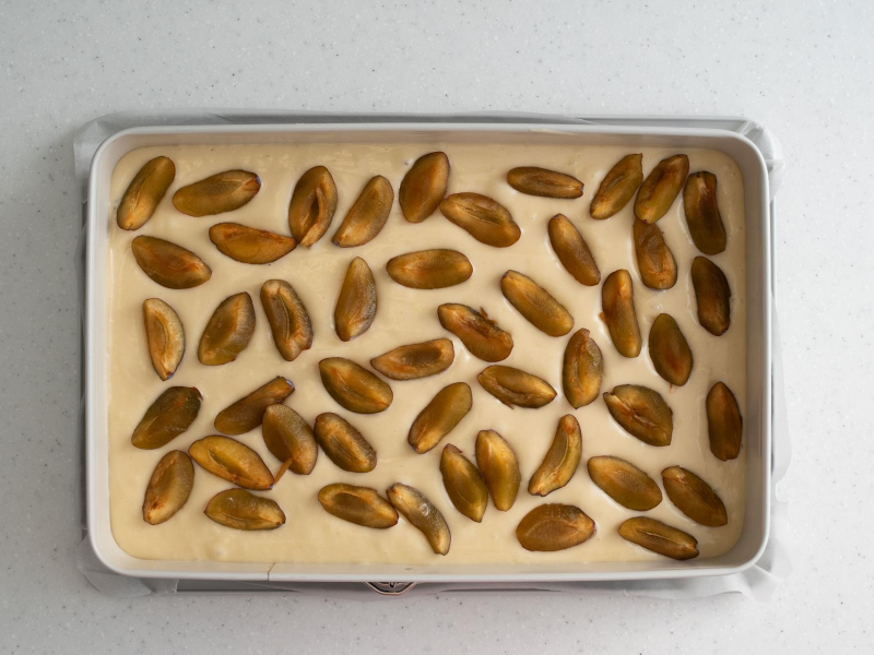 Ciasto jogurtowe ze śliwkami przełożone do prostokątnej formy.