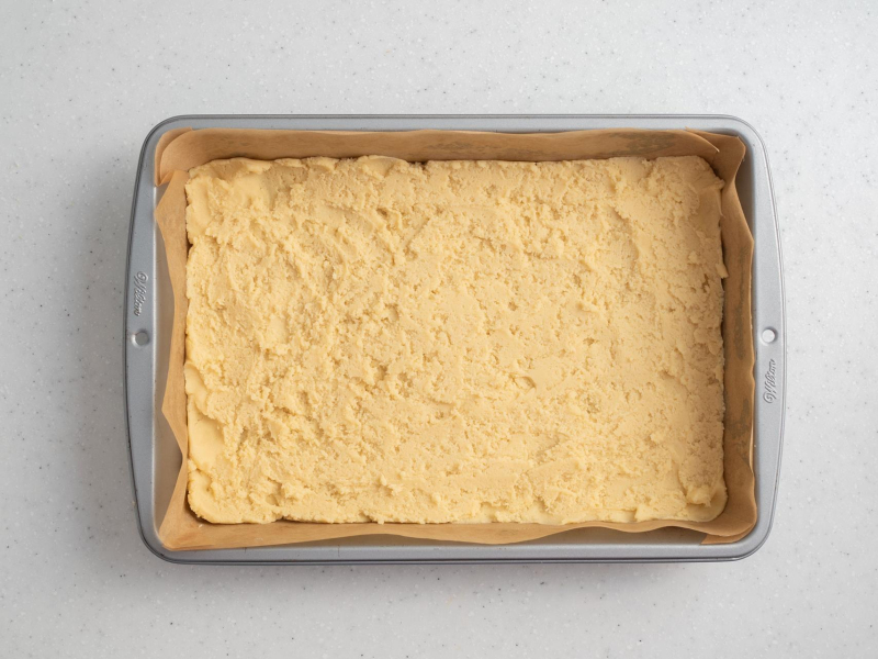 w formie do pieczenia wyłożonej papierem do pieczenia wyłożony spód ciasta do sernika z mlekiem w robocie