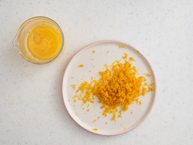 Na talerzyku starta skórka z pomarańczy. Obok sok z pomarańczy.