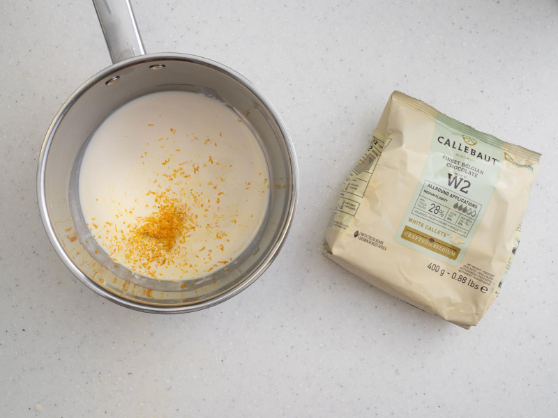 Na blacie kuchennym garnek ze śmietanką i skórką z pomarańczy. Obok opakowanie czekolady.