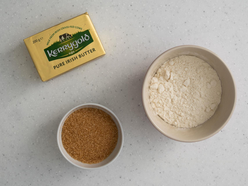 Na blacie kuchennym kostka masła. Obok cukier trzcinowy i mąka pszenna.