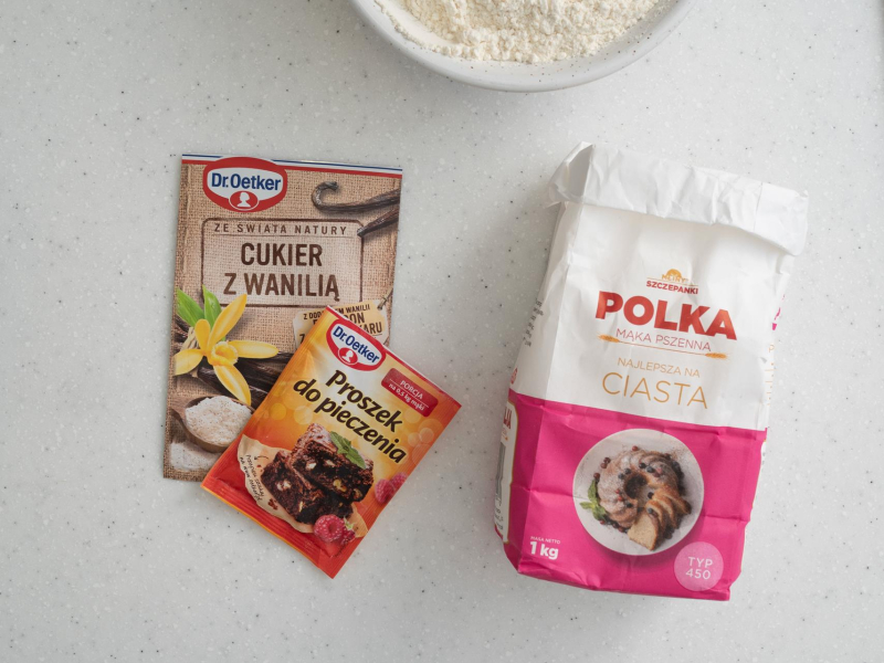 Na blacie kuchennym opakowanie mąki, cukru z wanilią i proszku do pieczenia.