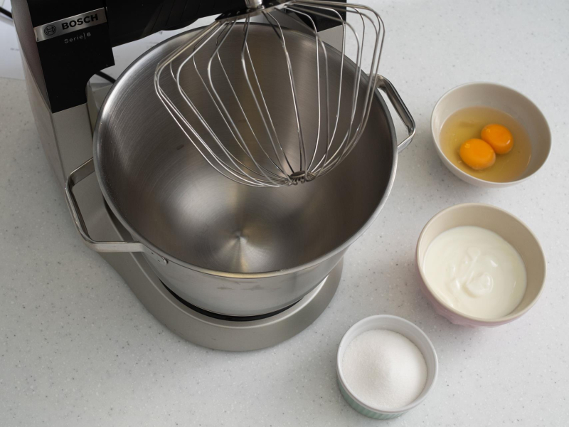 Robot kuchenny z końcówką do ubijania. W miseczkach jajka, mąka oraz cukier.