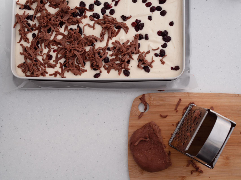 w dużej blaszce sernik piernikowy z żurawiną przed pieczeniem obok deska drewniana z tarką