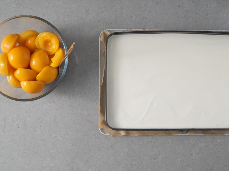 W misce po艂贸wki brzoskwi艅, Obok blacha z przygotowanym ciastem.