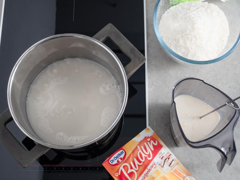 na kuchence garnek z mlekiem kokosowym, obok w naczyniu wymieszany budyń Dr. Oetkera