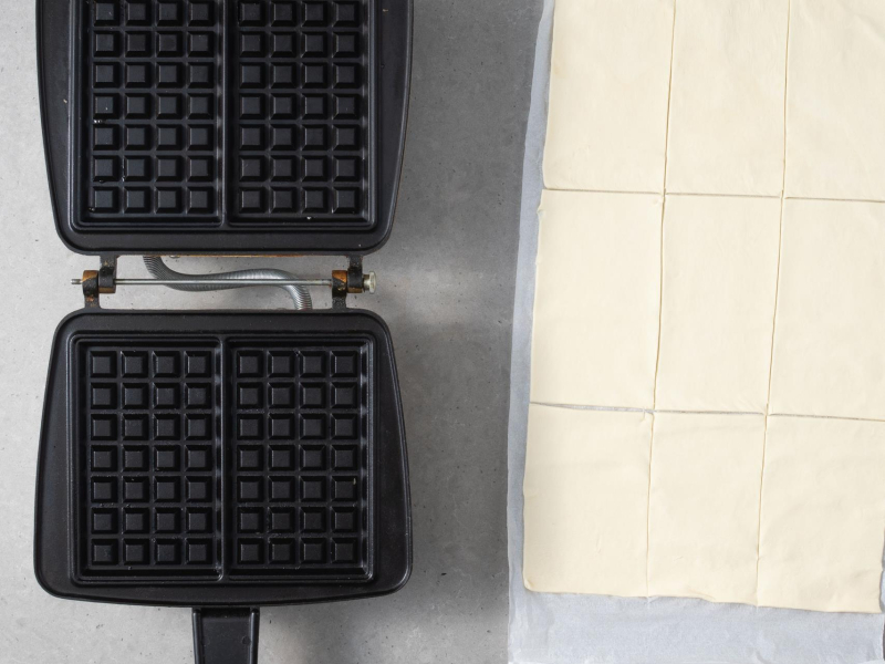 Na blacie kuchennym gofrownica. Obok pokrojone ciasto kruche na 9 kawałków/