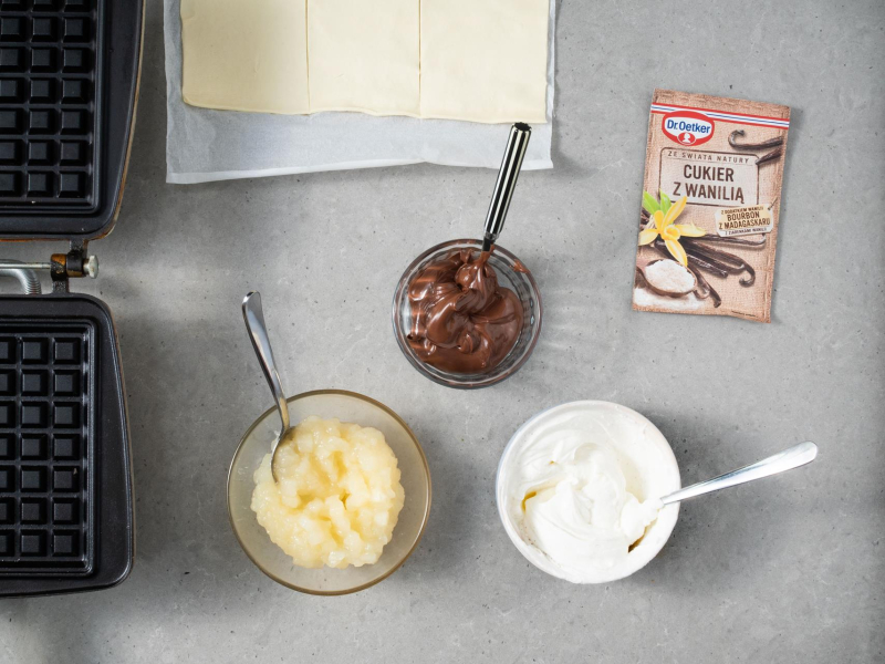 Przygotowane nadzienia do gofrów na blacie kuchennym:: serek  śmietankowy, nutella, prażone jabłka oraz cukier z wanilią.