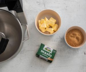 Na blacie kuchennym kostka masła oraz cukier trzcinowy w miseczce.