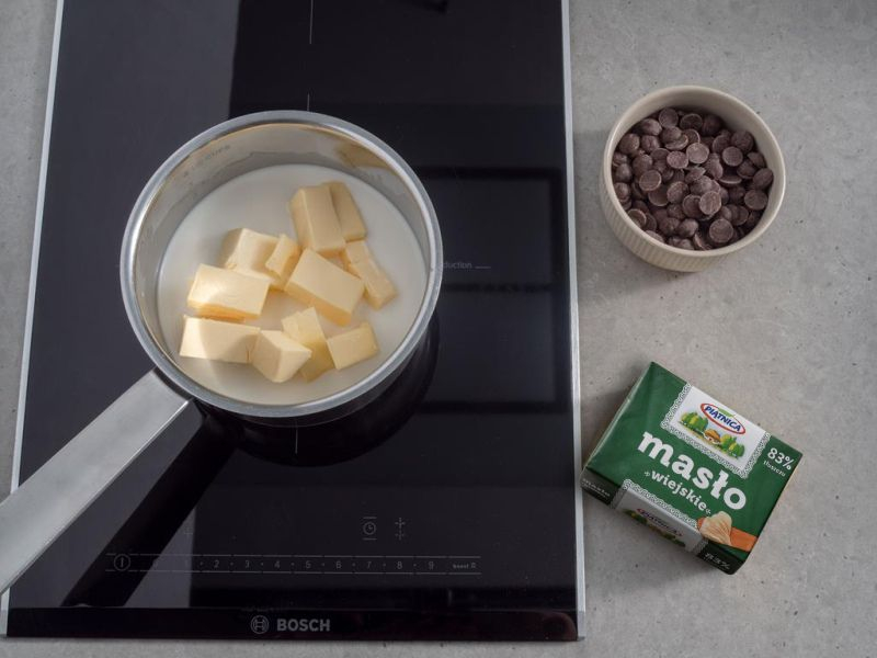 na kuchence indukcyjnej bosch w rondelku mleko z masłem, obok w miseczce kaletki czekolady
