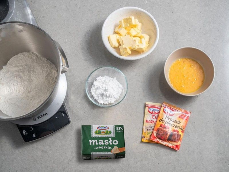 W misie mąka psklasycznego Lurpakzenna. Obok miseczka z jajkami, masłem oraz opakowanie masła i proszek do pieczenia Dr. Oetkera.