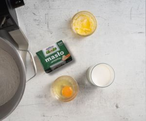 Na blacie kuchennym opakowanie masła, jajko, mleko oraz masło w miseczkach.