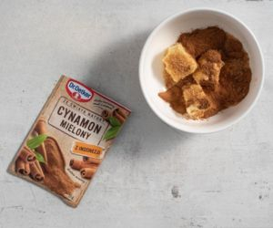 Na blacie kuchennym opakowanie masła, cynamon w opakowaniu, a w miseczce masło wymieszane z cukrem i cynamonem.