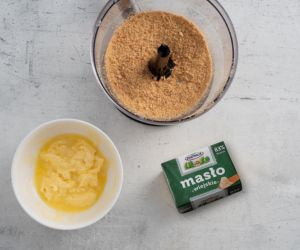 Zblendowane ciasteczka w pojemniku blendera ręcznego. Obok rozpuszczone masło.