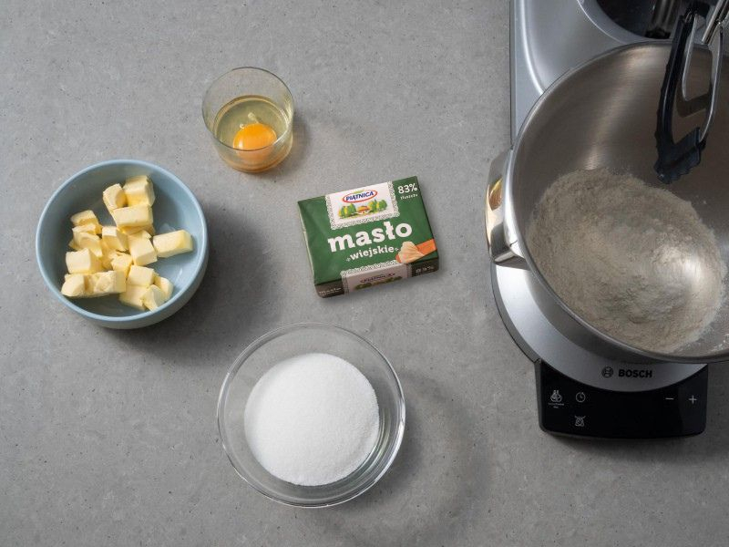 w misie robota kuchennego bosch przesiana mąka i cukier puder obok masło i jajko do  tarty