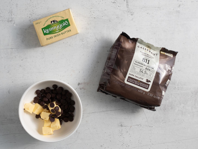 Na blacie kuchennym opakowanie czekolady i kostka masła. W miseczce oba składniki razem.