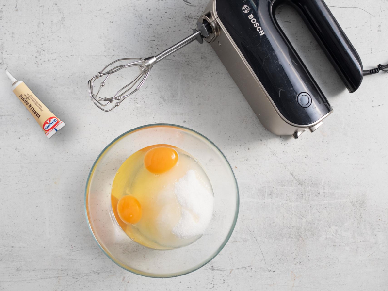 Na blacie kuchennym mikser ręczny. Obok opakowanie pasty z wanilii i miseczka z cukrem i jajkami.