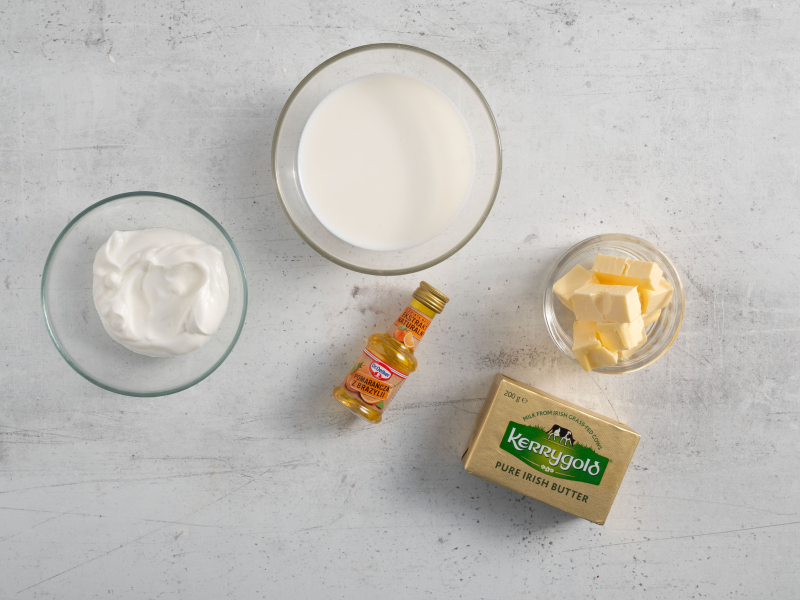 Na blacie kuchennym w miseczkach: mleko, jogurt, pokrojone masło w kostce oraz ekstrakt pomarańczowy.