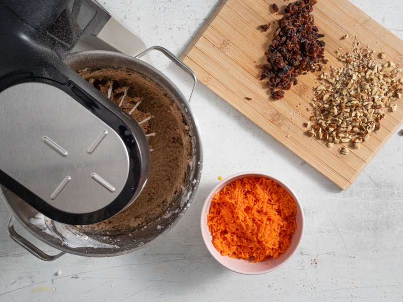 W misce starta marchewka. Na desce pokrojone orzechy i rodzynki.