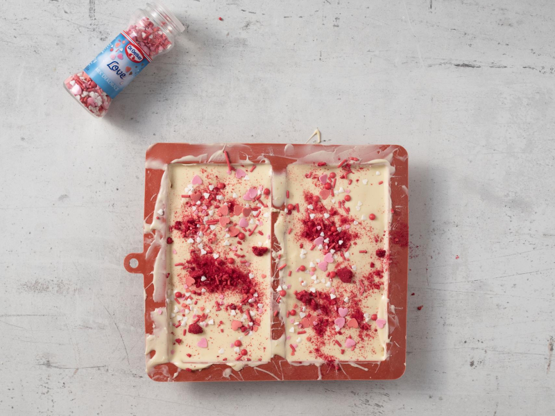 Gotowe tabliczki czekolady posypane liofilizowanymi malinami oraz posypką cukrową.