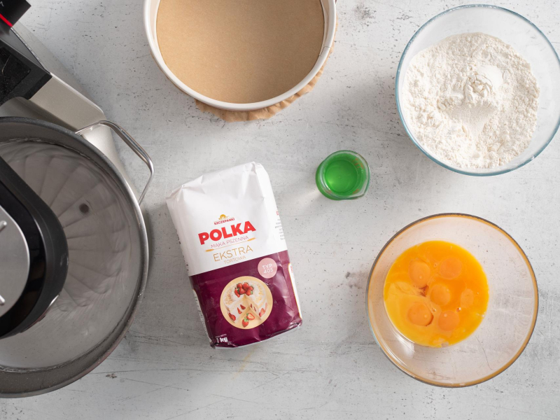 Na blacie opakowanie mąki, obok w miseczce żołtka, mąka, woda oraz przygotowana tortownica.