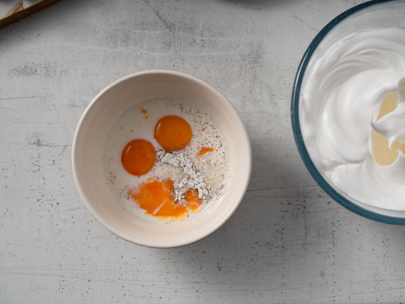 w miseczce żółtka i składniki na puszyste pankejki obok w misce ubite białka