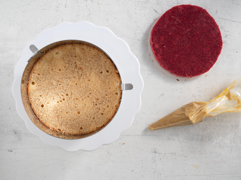 Blat nasączony cienką warstwą kremu. Obok żelka i krem pistacjowy w rękawie.