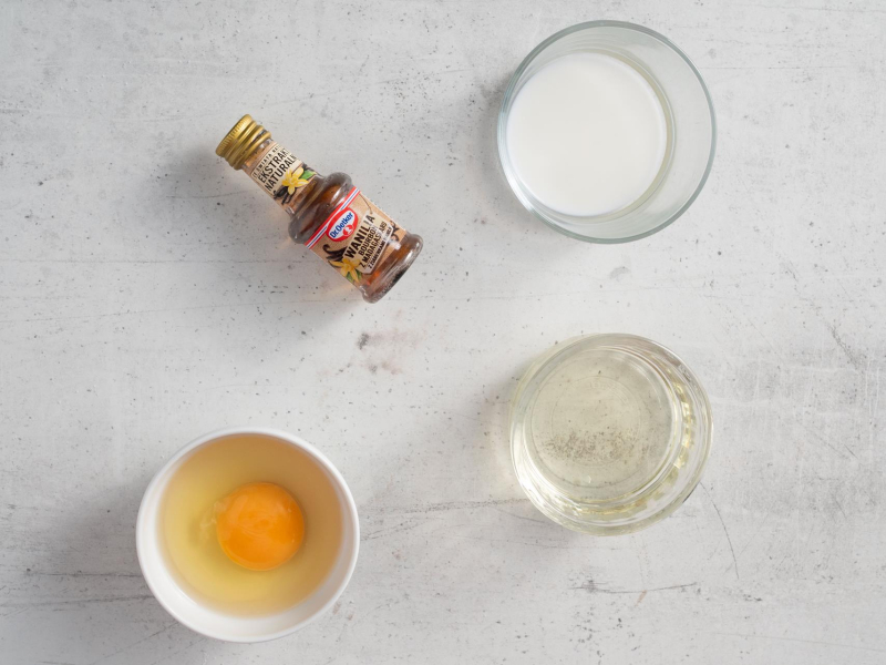 Butelka ekstraktu z wanilii, jajko w miseczce, olej oraz mleko.
