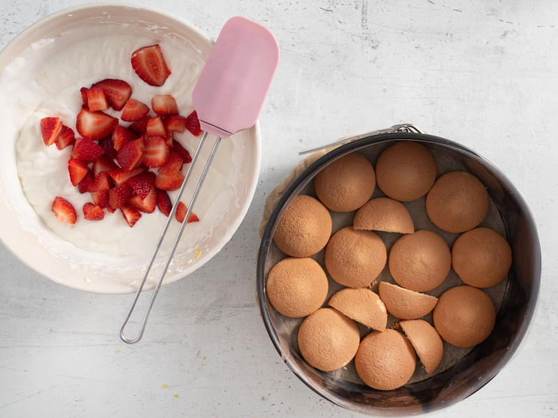 Tortownica wyłożona biszkoptami, a obok masa skyrnikowa z truskawkami.