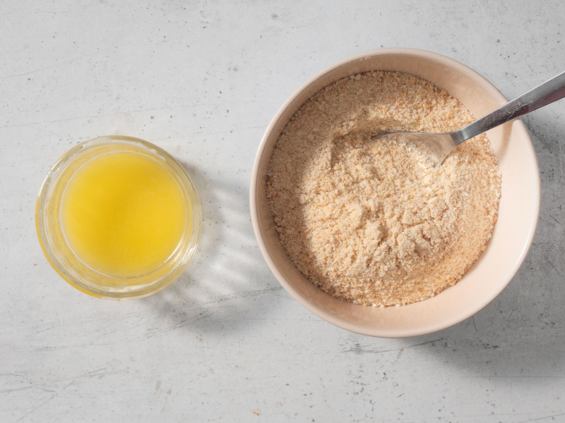 pokruszone herbatniki w miseczce, obok roztopione masło