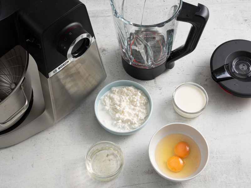 Na blacie kuchennym w miseczkach: serek wiejski, jajka, mleko i olej.