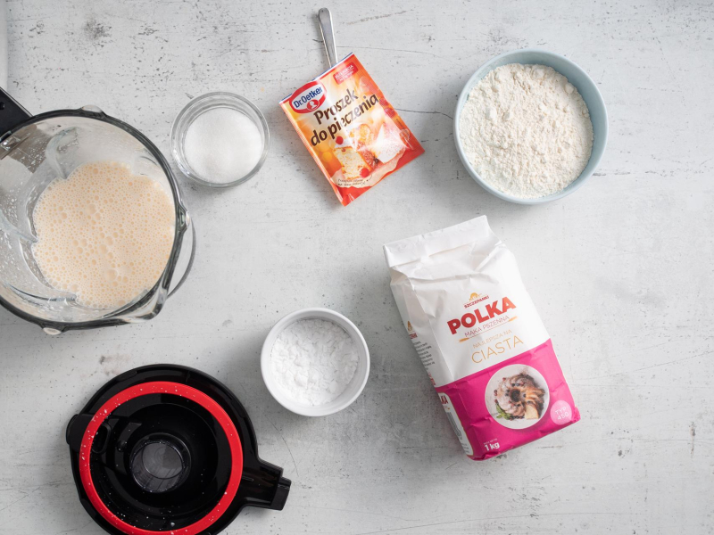 W blenderze kielichowym zblendowane mokre sk艂adniki. Obok opakowanie m膮ki pszennej, proszku do pieczenia. A w miseczkach m膮ka, m膮ka ziemniaczana i cukier.