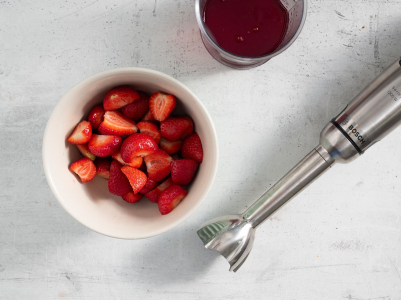 Pokrojone truskawki w miseczce. A obok blender ręczny.